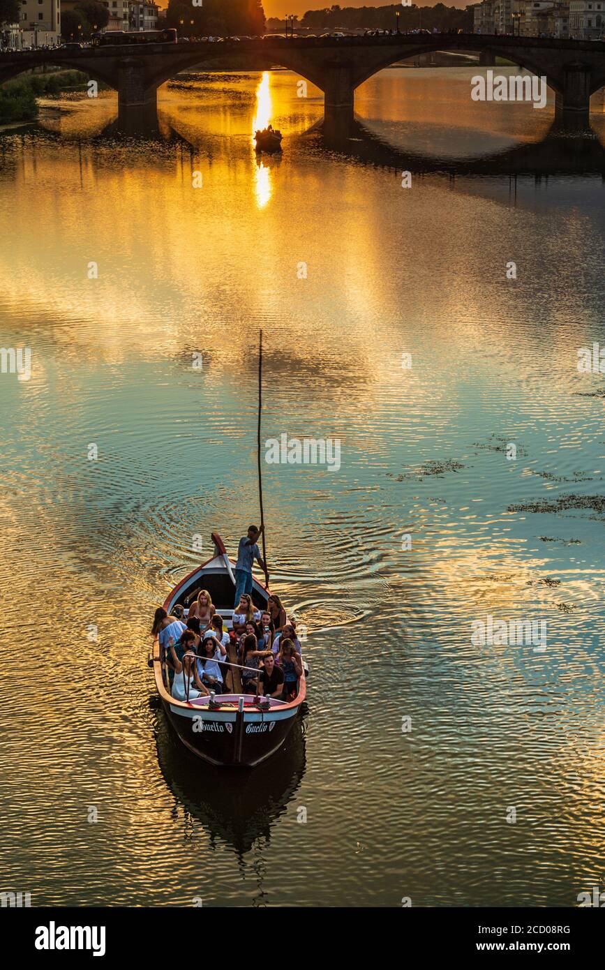 una piccola barca piena di turisti (il cosiddetto renaiolo) Galleggia sul fiume Arno di Firenze al tramonto Foto Stock