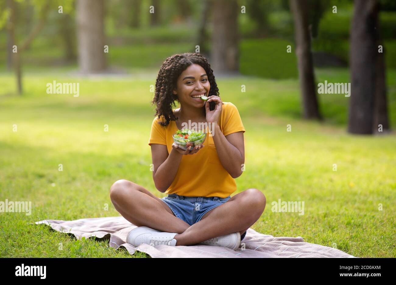 Alimentazione sana. Fit African American donna mangiare yummy insalata di verdure dalla ciotola al parco Foto Stock