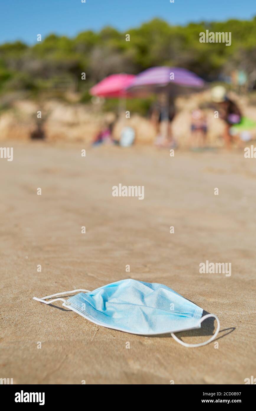 primo piano di una maschera chirurgica blu usata gettata sulla sabbia bagnata della riva di una spiaggia Foto Stock
