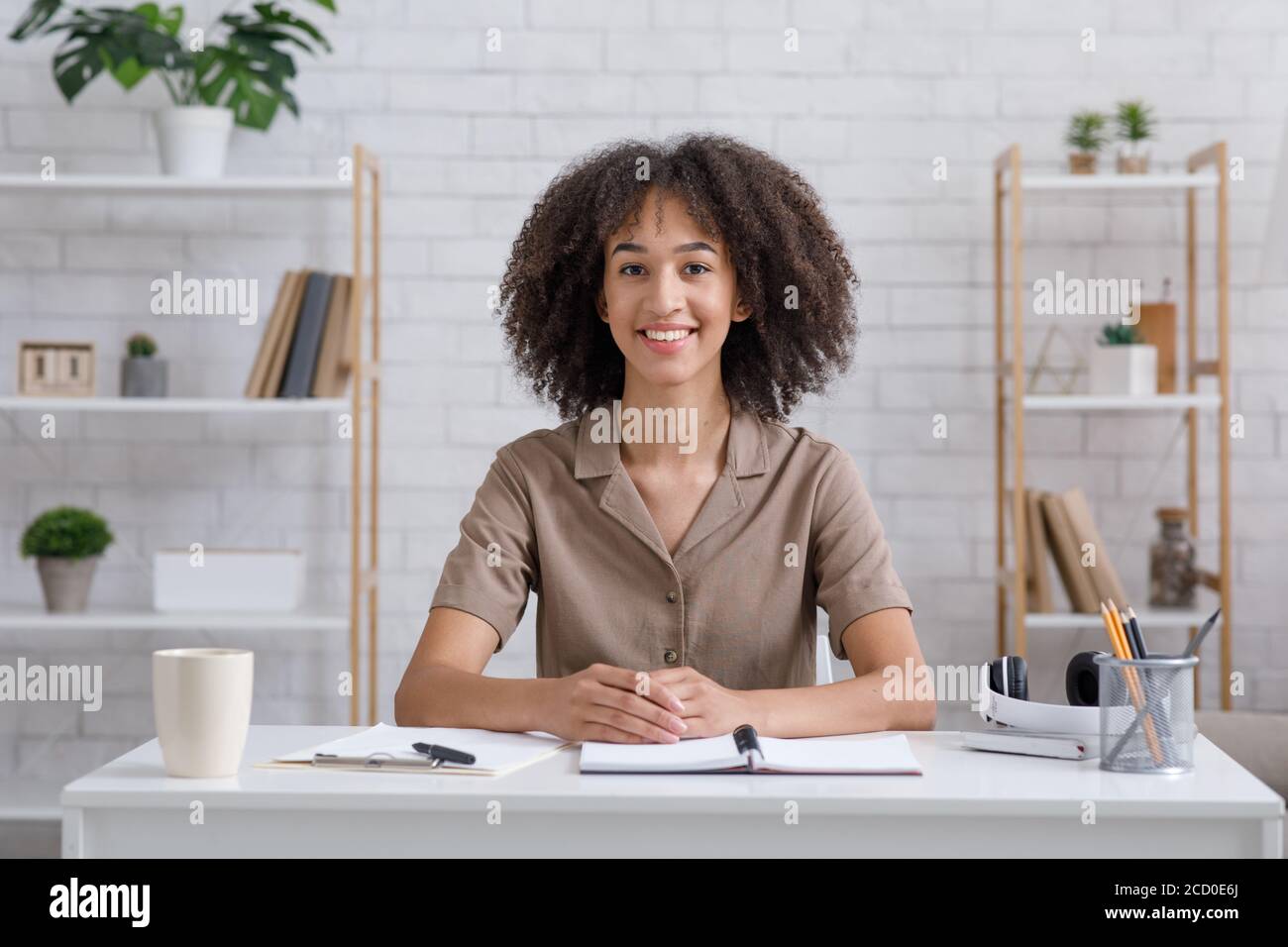 Lingua di apprendimento a distanza. Un insegnante sorridente si siede al tavolo, guarda la telecamera e comunica con gli studenti Foto Stock