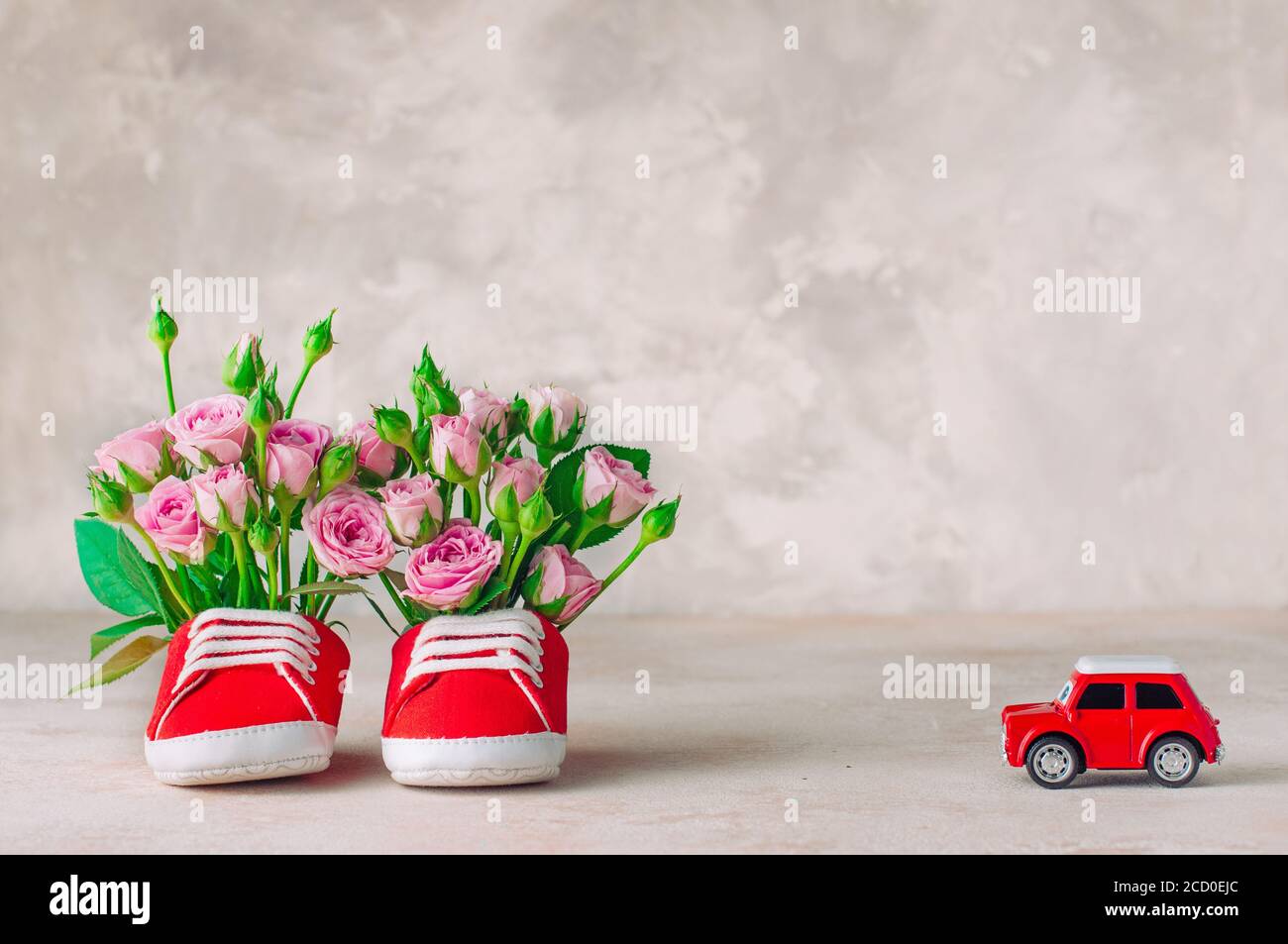 Paio di scarpe rosse per bambini riempite con fiori di rose e giocattoli per auto. Spazio vuoto per il testo. Foto Stock