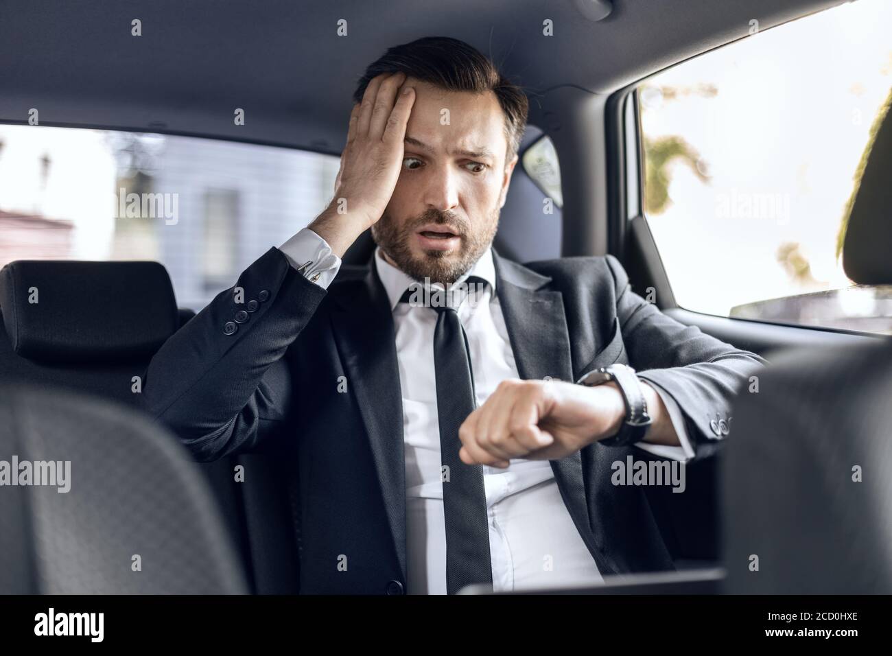 Uomo d'affari preoccupato guardando il suo orologio mentre si va in auto Foto Stock