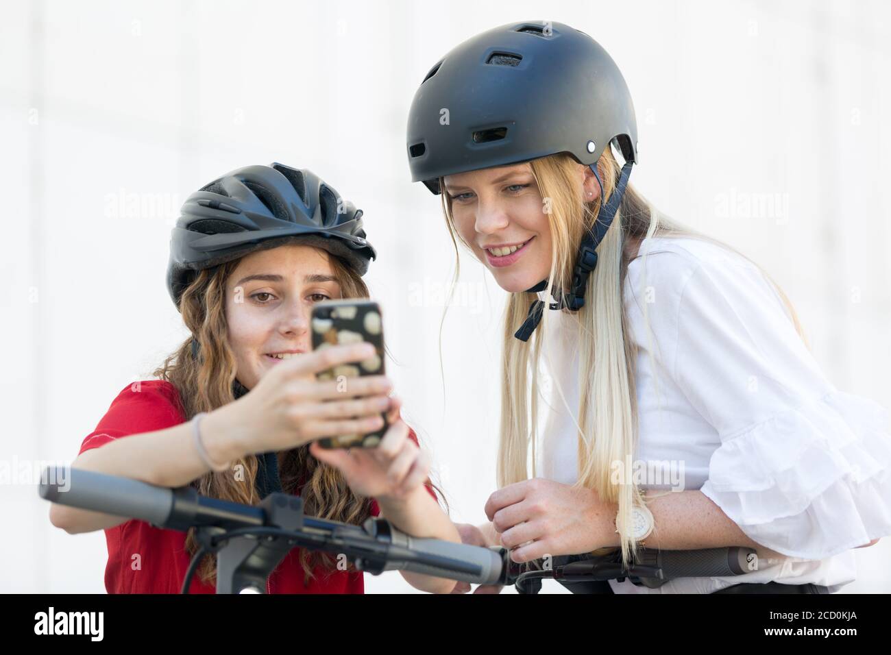 Ragazze adolescenti che utilizzano l'applicazione mobile per sbloccare e noleggiare scooter elettrici a noleggio pubblico in ambiente urbano. Moderno ed ecologico Foto Stock