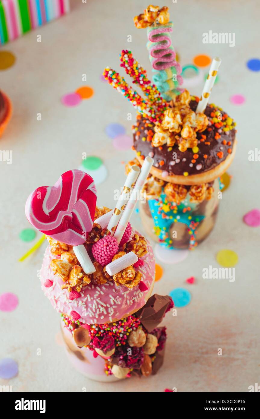 Vista dall'alto di due frullati di freak con ciambelle, popcorn e dolci sullo sfondo della festa; messa a fuoco selettiva sulla frolla di lampone. Foto Stock