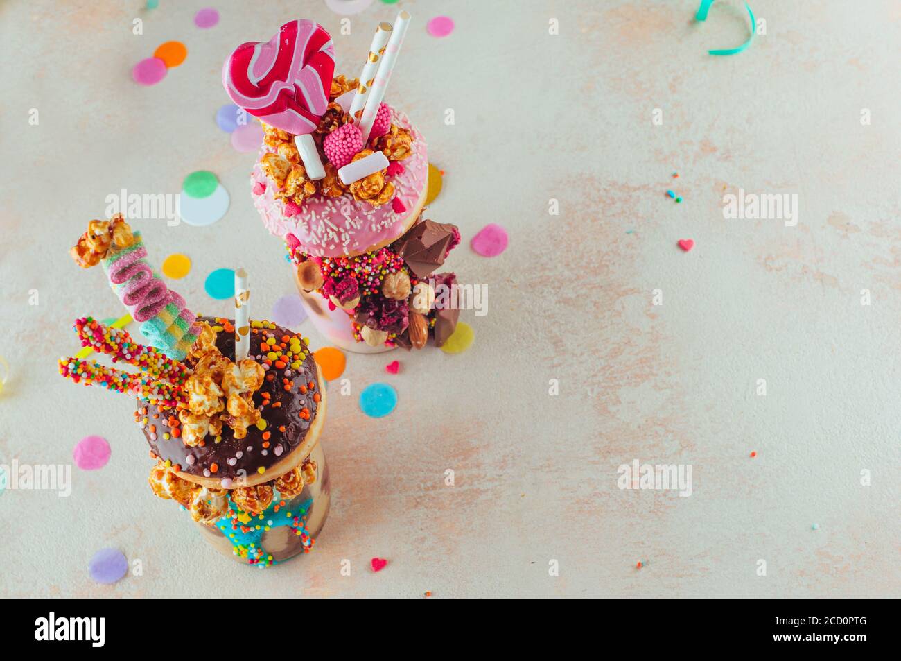 Concetto di festa dei bambini: Vista dall'alto di due frullati di freak con ciambelle, popcorn al caramello e dolci sullo sfondo della festa con spazio vuoto per il testo Foto Stock