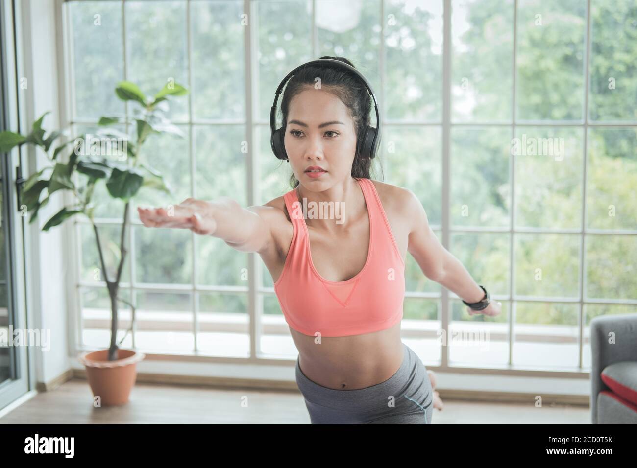 Giovane donna asiatica che fa esercizi di yoga a casa, in piedi da una gamba in equilibrio, respirazione e relax. Foto Stock