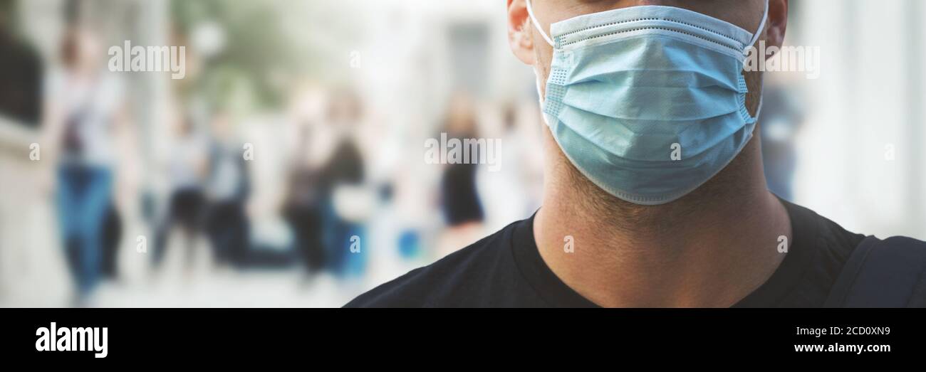 uomo che indossa una maschera medica a affollata strada della città durante la pandemia del virus. spazio di copia banner Foto Stock