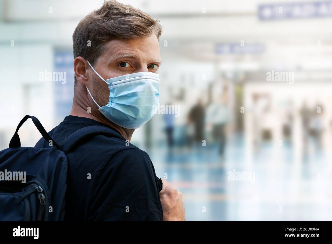 giovane uomo che indossa una maschera usa e getta al terminal dell'aeroporto durante pandemia virale Foto Stock