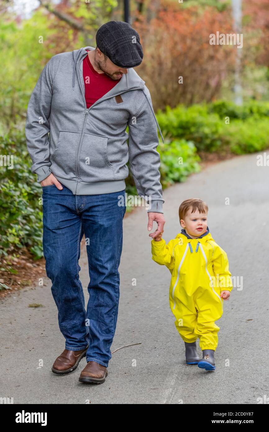 Padre che tiene le mani con la giovane figlia mentre si prende una passeggiata nel parco; North Vancouver, British Columbia, Canada Foto Stock