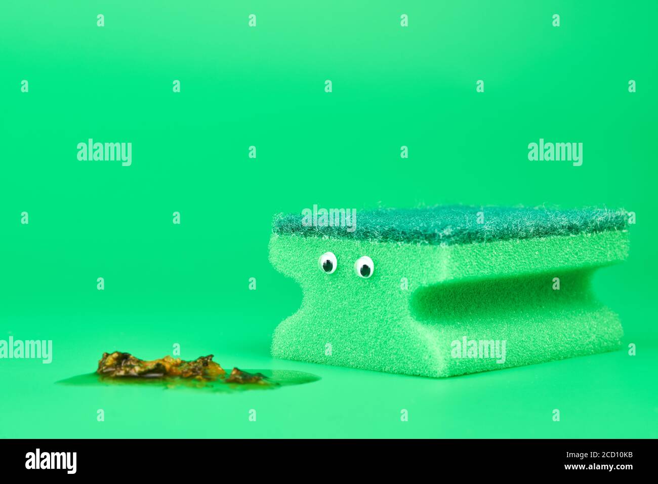 Spugna verde divertente con gli occhi per la pulizia, la pulizia e il lavaggio dei piatti. Concetto di divertimento. Spugna biadesivo morbida e dura. Sfondo verde minimo, Foto Stock