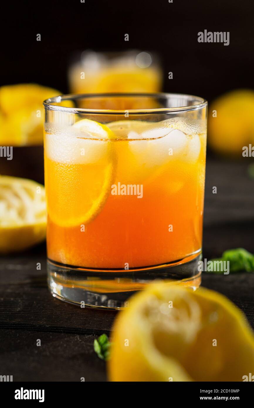 Vista verticale sul tè freddo al limone su sfondo scuro. Una rinfrescante bevanda estiva fatta di limone spremuto a mano fresco mescolato con tè nero freddo, ghiaccio e zucchero. Foto Stock