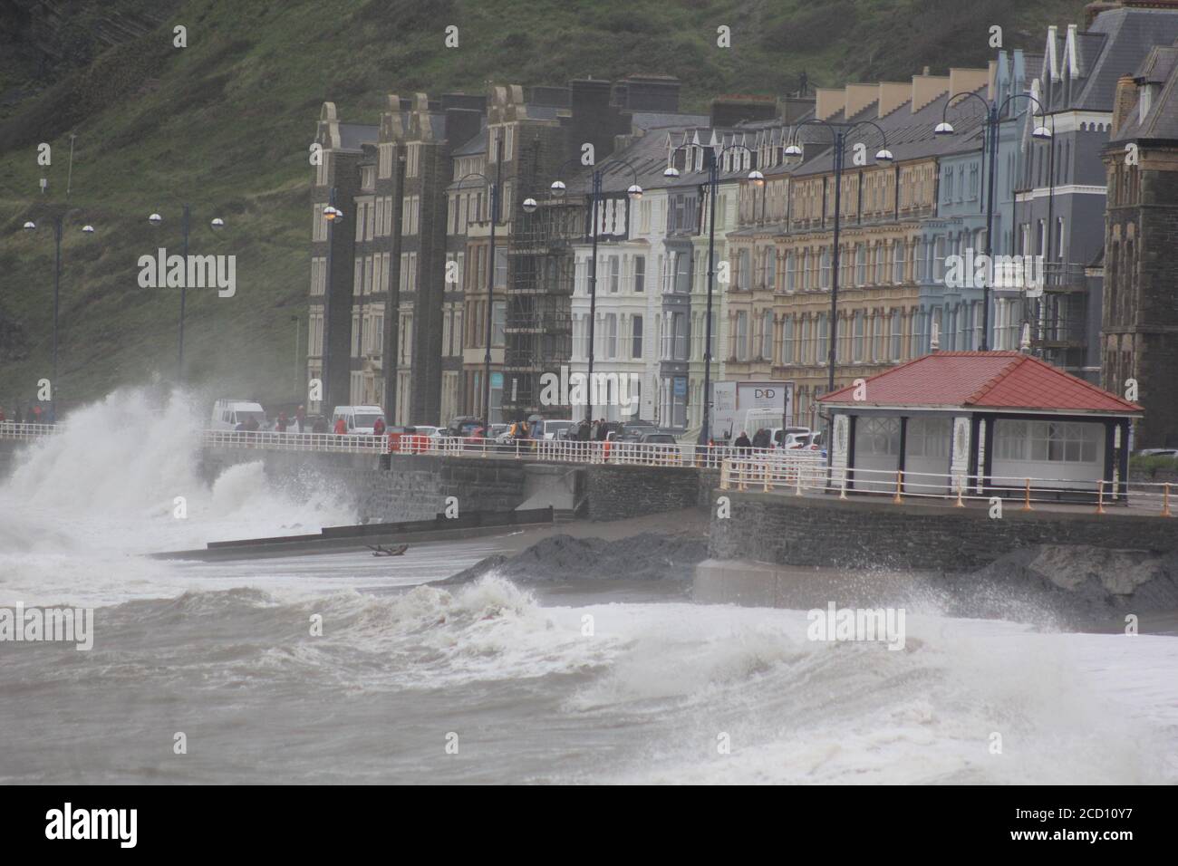 Aberystwyth Wales UK Weather 25 agosto 2020 : forti piogge e venti di Gale Force battter regioni costiere del Galles, forti venti guidare in enormi onde che sconfinano contro le difese marine di Aberystwyth. I vacanzieri coraggiosi venti di forza gale durante una passeggiata pomeridiana tempesta lungo la passeggiata, Credit: mike davies/Alamy Live News Foto Stock