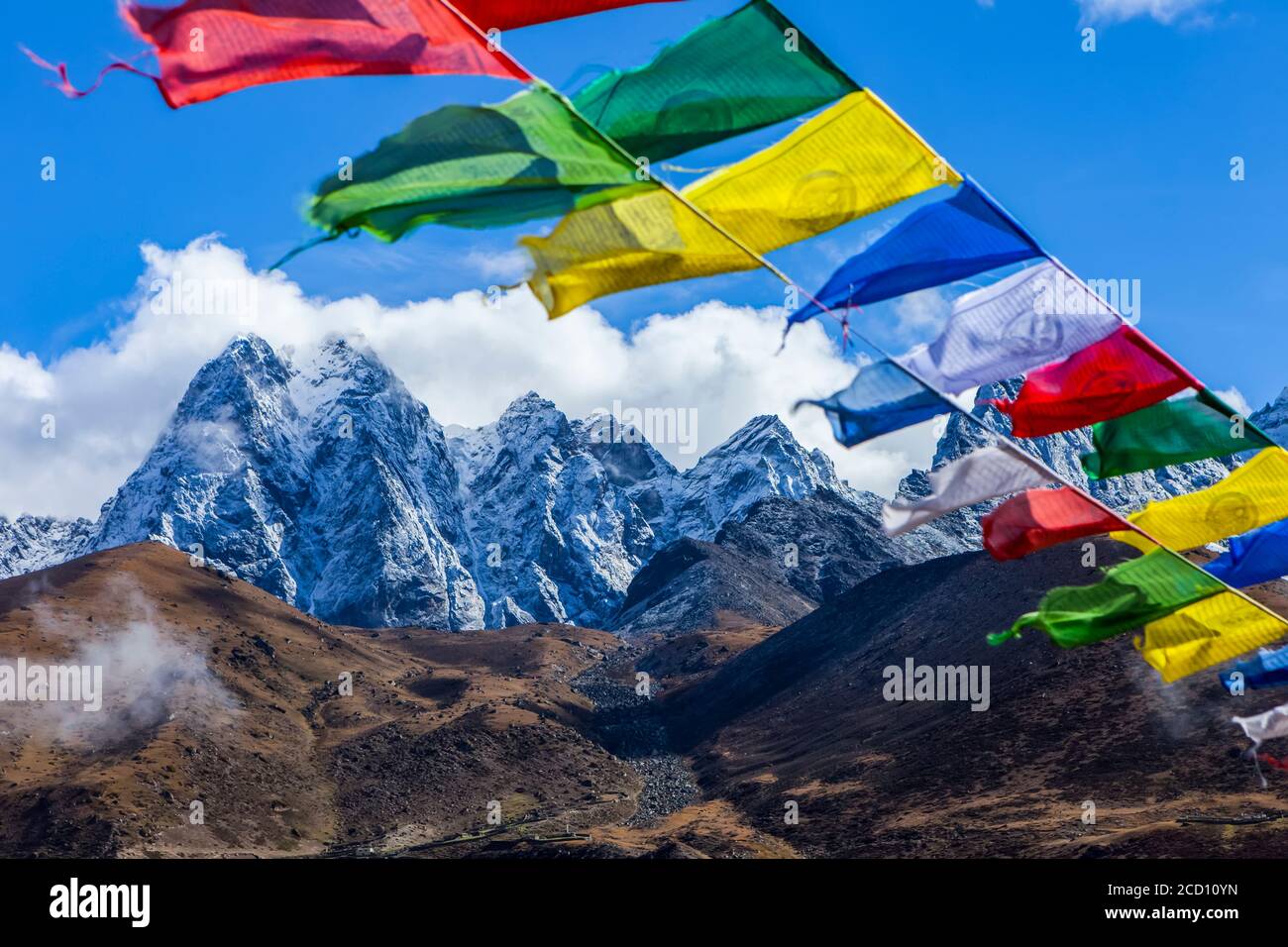 Bandiere di preghiera colorate flap nel vento, con recentemente spolverato, neve-coperto cime Himalayan, e tundra autunno colorato sullo sfondo in Sol... Foto Stock