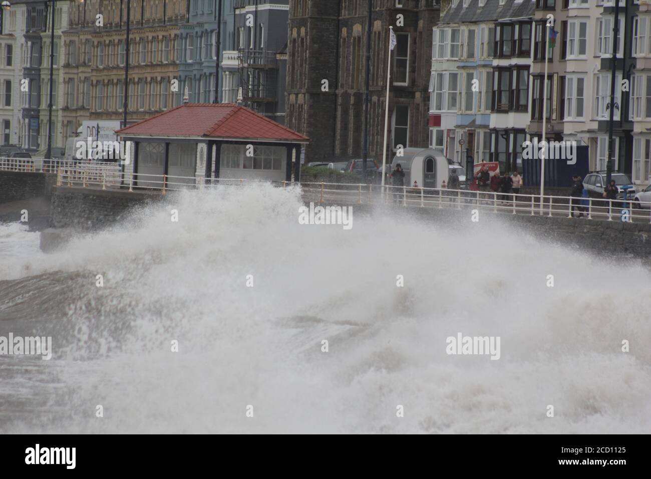 Aberystwyth Wales UK Weather 25 agosto 2020 : forti piogge e venti di Gale Force battter regioni costiere del Galles, forti venti guidare in enormi onde che sconfinano contro le difese marine di Aberystwyth. I vacanzieri coraggiosi venti di forza gale durante una passeggiata pomeridiana tempesta lungo la passeggiata, Credit: mike davies/Alamy Live News Foto Stock