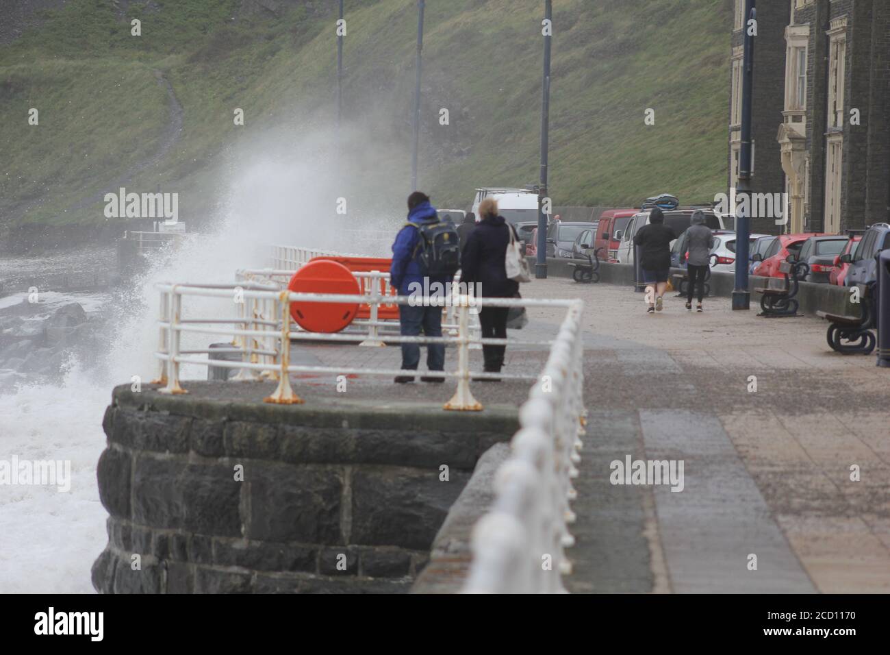 Aberystwyth Wales UK Weather 25 agosto 2020 : forti piogge e venti di Gale Force battter regioni costiere del Galles, forti venti guidare in enormi onde che sconfinano contro le difese marine di Aberystwyth. I vacanzieri coraggiosi venti di forza gale durante una passeggiata pomeridiana tempesta lungo la passeggiata, Credit: mike davies/Alamy Live News Foto Stock