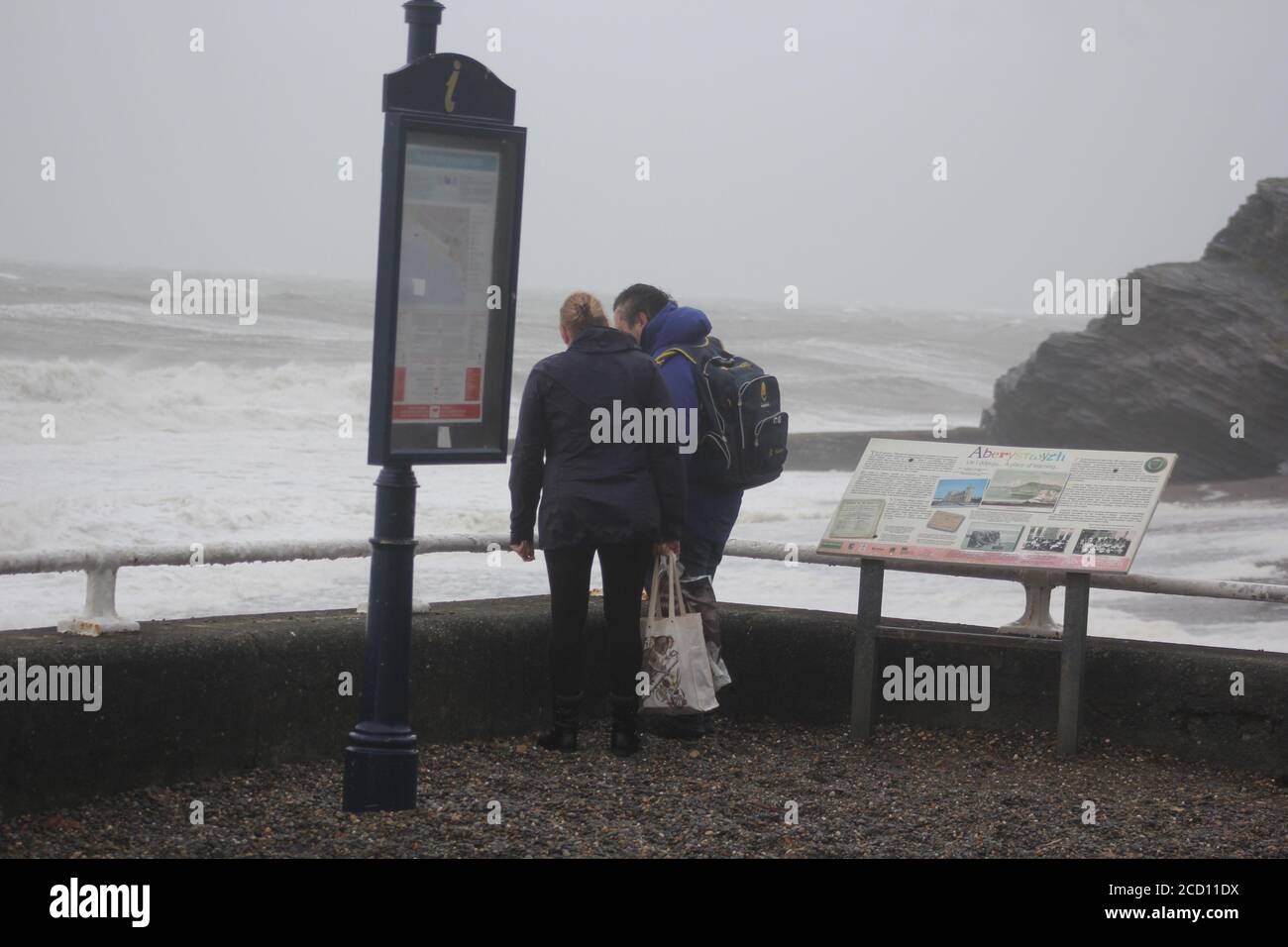Aberystwyth Wales UK Weather 25 agosto 2020 : forti piogge e venti di Gale Force battter regioni costiere del Galles, forti venti guidare in enormi onde che sconfinano contro le difese marine di Aberystwyth. I vacanzieri coraggiosi venti di forza gale durante una passeggiata pomeridiana tempesta lungo la passeggiata, Credit: mike davies/Alamy Live News Foto Stock