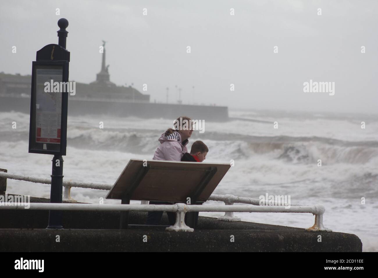 Aberystwyth Wales UK Weather 25 agosto 2020 : forti piogge e venti di Gale Force battter regioni costiere del Galles, forti venti guidare in enormi onde che sconfinano contro le difese marine di Aberystwyth. I vacanzieri coraggiosi venti di forza gale durante una passeggiata pomeridiana tempesta lungo la passeggiata, Credit: mike davies/Alamy Live News Foto Stock