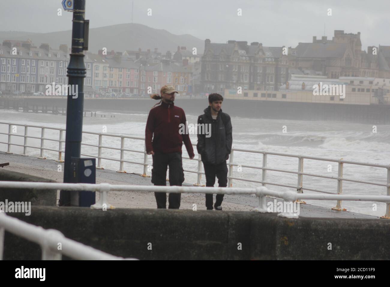 Aberystwyth Wales UK Weather 25 agosto 2020 : forti piogge e venti di Gale Force battter regioni costiere del Galles, forti venti guidare in enormi onde che sconfinano contro le difese marine di Aberystwyth. I vacanzieri coraggiosi venti di forza gale durante una passeggiata pomeridiana tempesta lungo la passeggiata, Credit: mike davies/Alamy Live News Foto Stock