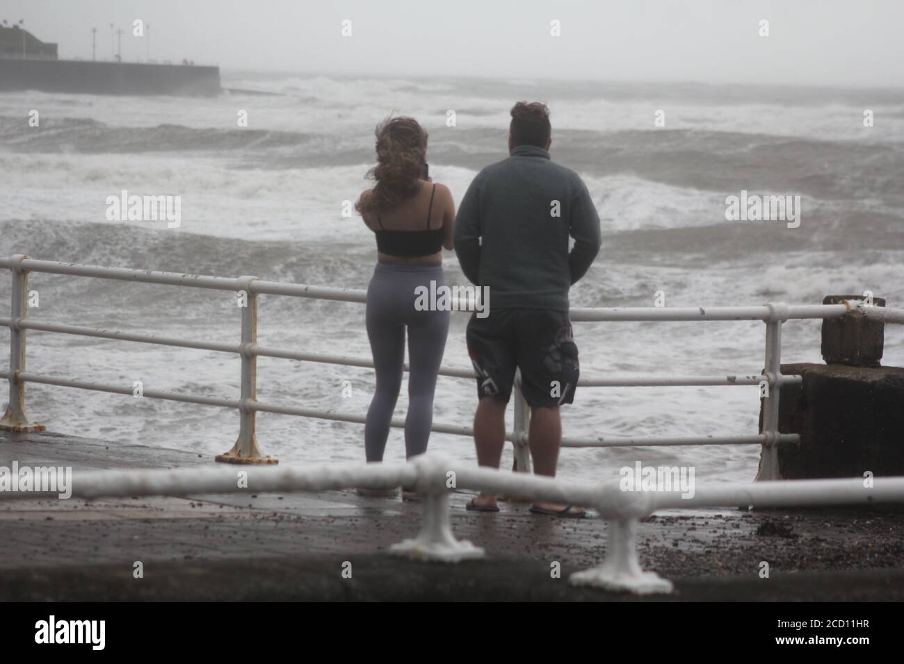 Aberystwyth Wales UK Weather 25 agosto 2020 : forti piogge e venti di Gale Force battter regioni costiere del Galles, forti venti guidare in enormi onde che sconfinano contro le difese marine di Aberystwyth. I vacanzieri coraggiosi venti di forza gale durante una passeggiata pomeridiana tempesta lungo la passeggiata, Credit: mike davies/Alamy Live News Foto Stock