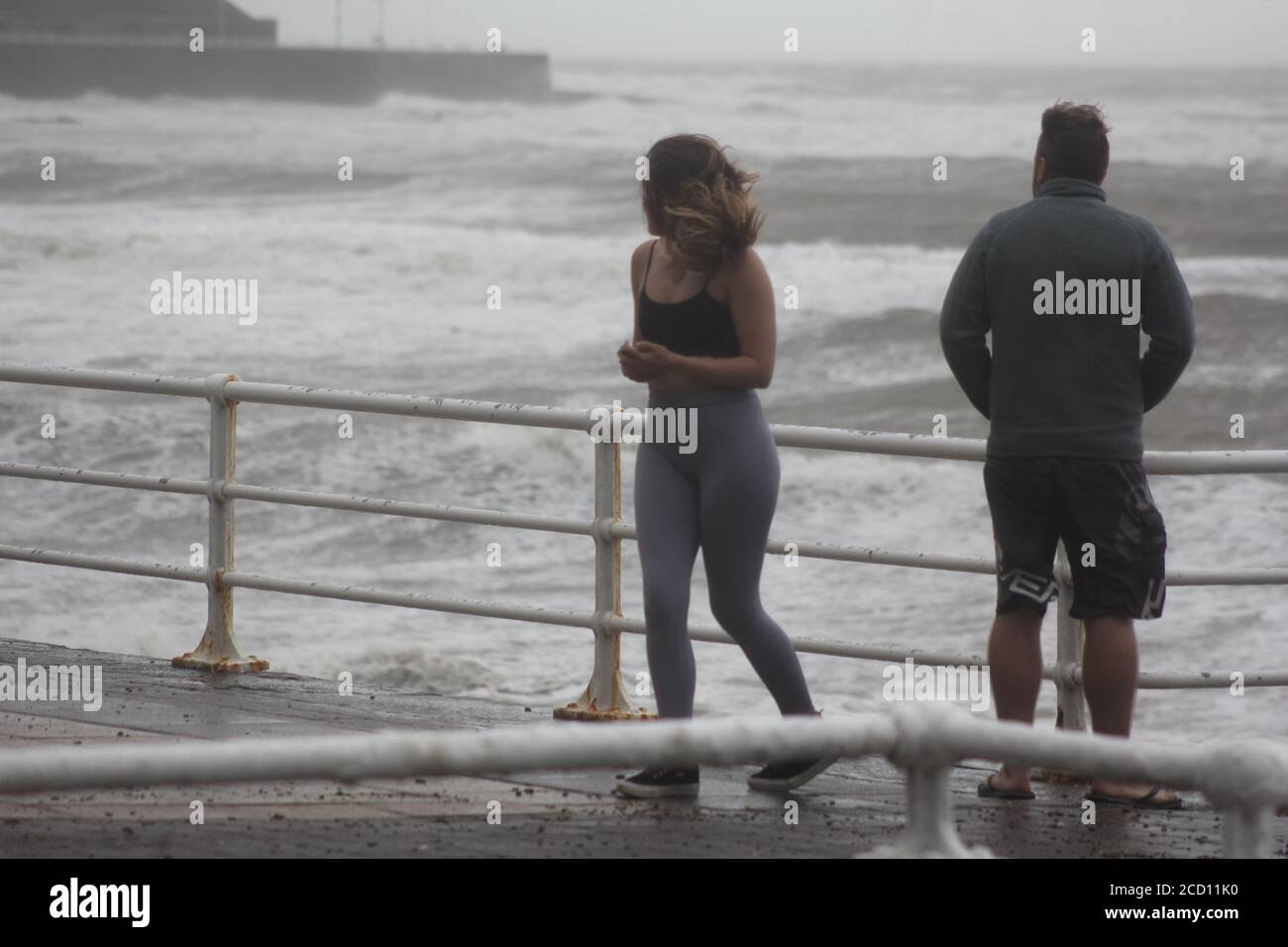 Aberystwyth Wales UK Weather 25 agosto 2020 : forti piogge e venti di Gale Force battter regioni costiere del Galles, forti venti guidare in enormi onde che sconfinano contro le difese marine di Aberystwyth. I vacanzieri coraggiosi venti di forza gale durante una passeggiata pomeridiana tempesta lungo la passeggiata, Credit: mike davies/Alamy Live News Foto Stock