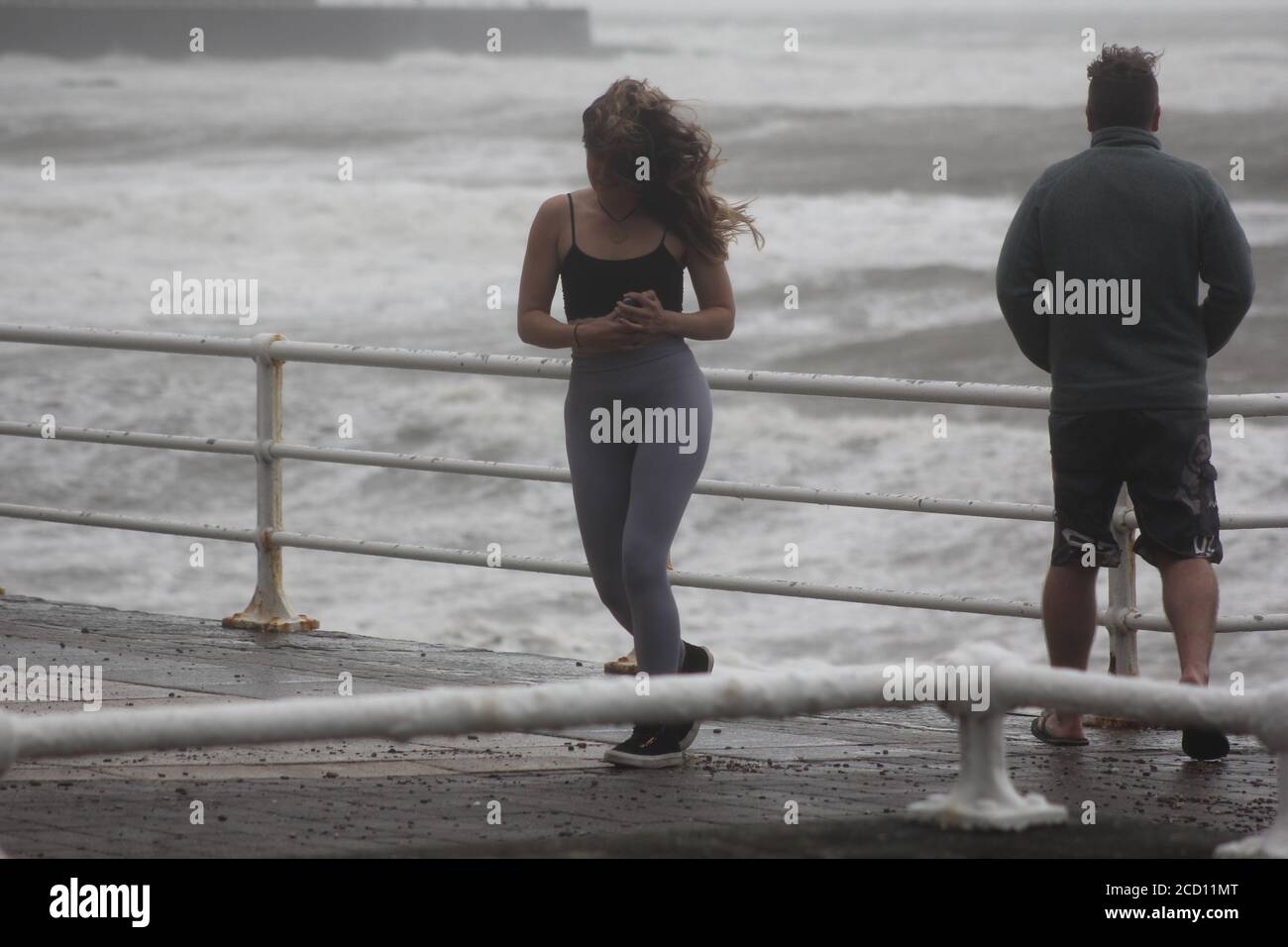 Aberystwyth Wales UK Weather 25 agosto 2020 : forti piogge e venti di Gale Force battter regioni costiere del Galles, forti venti guidare in enormi onde che sconfinano contro le difese marine di Aberystwyth. I vacanzieri coraggiosi venti di forza gale durante una passeggiata pomeridiana tempesta lungo la passeggiata, Credit: mike davies/Alamy Live News Foto Stock
