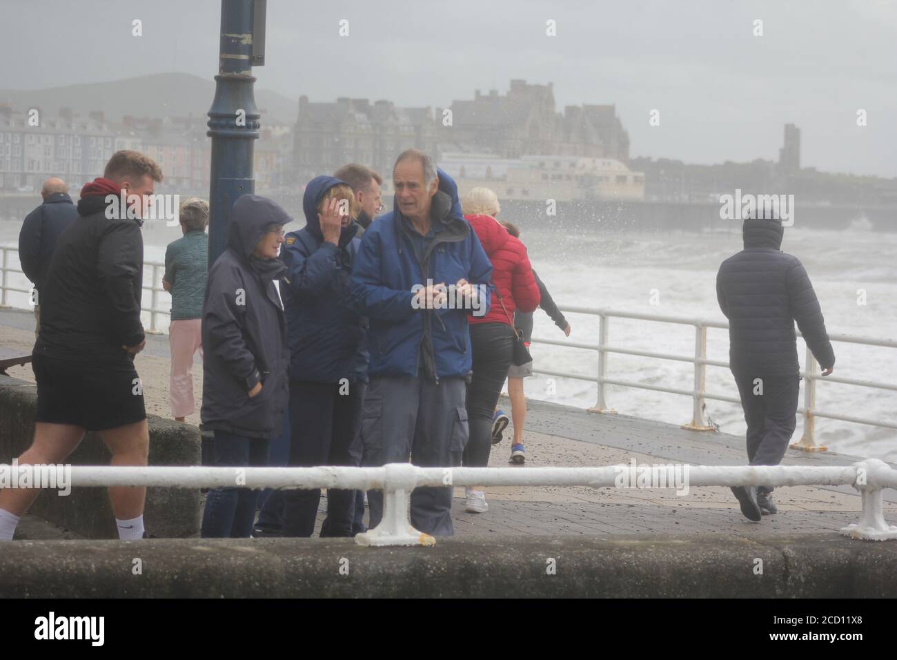Aberystwyth Wales UK Weather 25 agosto 2020 : forti piogge e venti di Gale Force battter regioni costiere del Galles, forti venti guidare in enormi onde che sconfinano contro le difese marine di Aberystwyth. I vacanzieri coraggiosi venti di forza gale durante una passeggiata pomeridiana tempesta lungo la passeggiata, Credit: mike davies/Alamy Live News Foto Stock