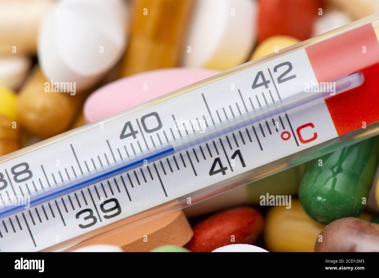 Termometro che indica una temperatura superiore a 40 °C. Sfondo di compresse e pillole di diversi tipi e colori Foto Stock