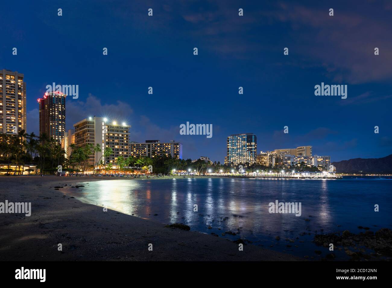 Waikiki al tramonto, con edifici illuminati e tranquillo lungomare; Honolulu, Oahu, Hawaii, Stati Uniti d'America Foto Stock