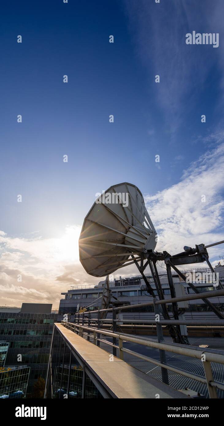 Parabola satellitare in un moderno edificio d'ufficio, cielo blu e sole tramontante. Concetto di comunicazione a lunga distanza Foto Stock