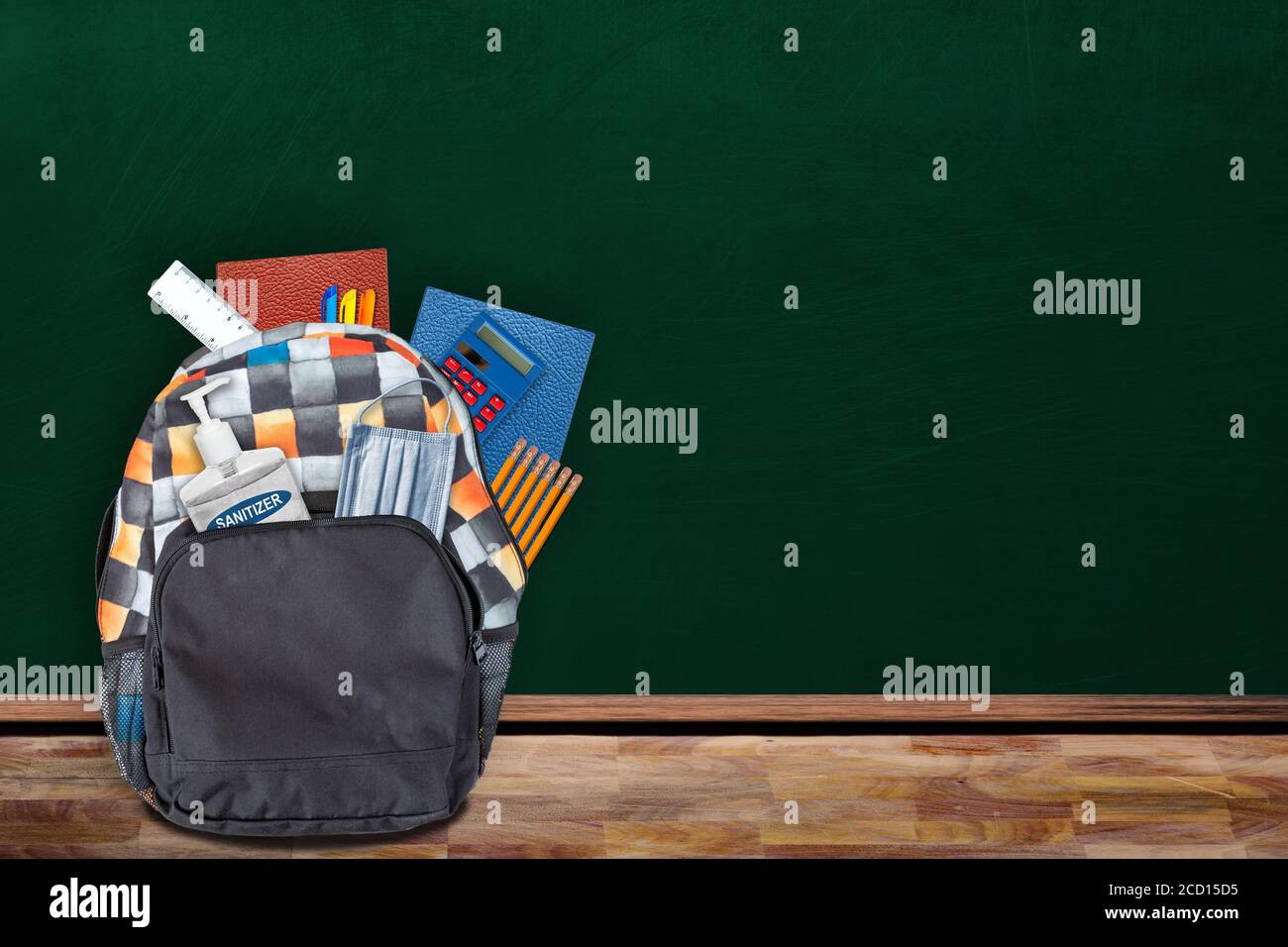 Concetto di educazione "back-to-School" nella nuova normale impostazione in classe che mostra lo zaino imbottito di cancelleria, igienizzatore per le mani e maschera facciale sul tavolo w Foto Stock