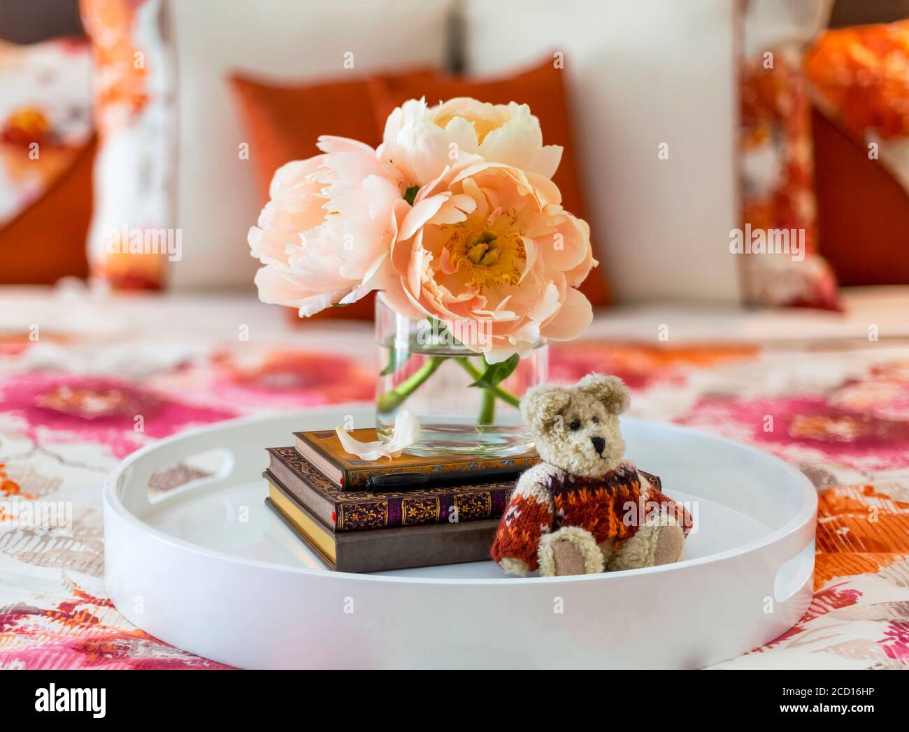 Bouquet di peonie colorate di pesca, libri e piccoli orsetto di lana un vassoio da letto sulla parte superiore di un letto con fiori biancheria da letto a motivi geometrici Foto Stock