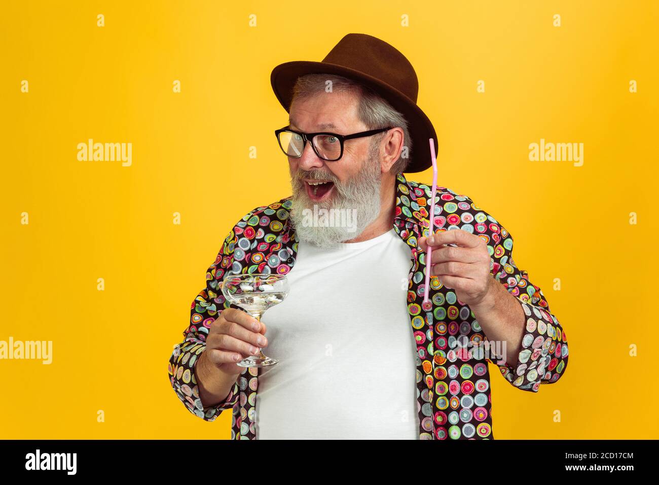 È il momento di bere. Ritratto di uomo hipster senior in occhiali isolati su sfondo giallo studio. Concetto di stile di vita per anziani con tecnologia e gioia. Colori alla moda, per sempre giovani. CopySpace per il tuo annuncio. Foto Stock