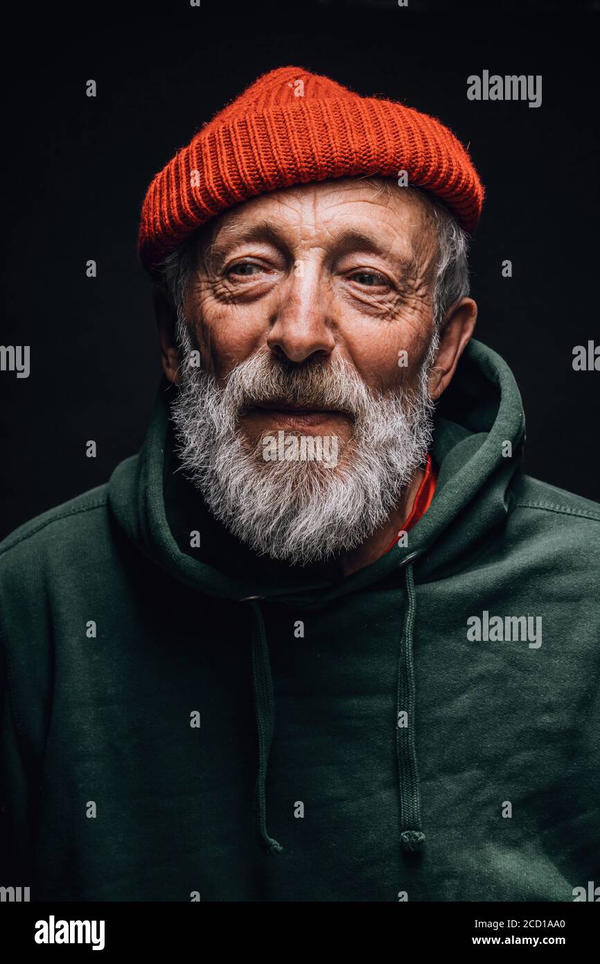 Ritratto di vecchio uomo bearded in cappello arancione con viso rugoso e occhi stanchi esperti che esprimono positività e gioia, ponendosi isolato sopra Foto Stock
