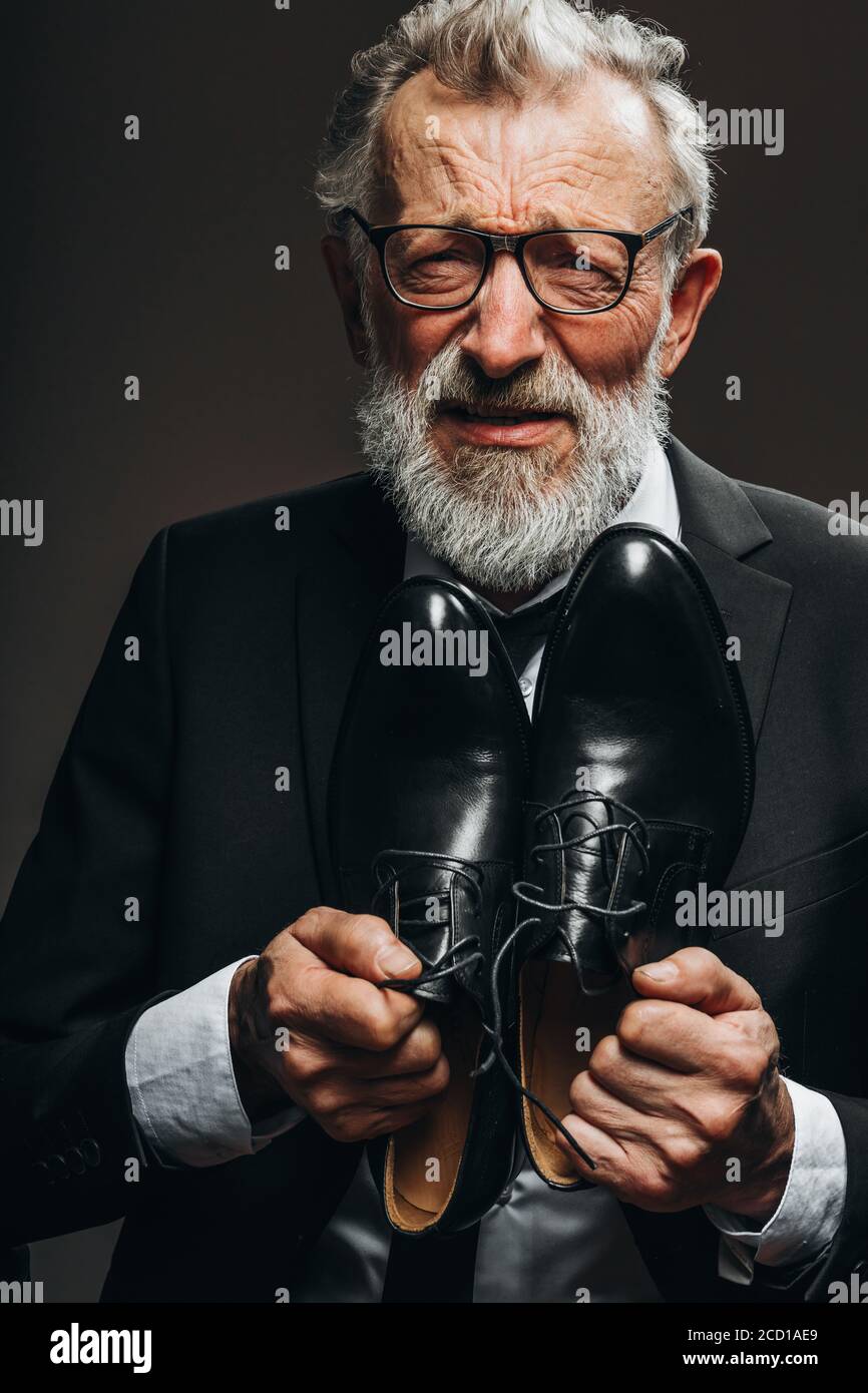 Infelice miserabile vecchio uomo d'affari in bancarotta che chiede di non privarlo dell'ultimo, tenendo le sue scarpe costose sul petto Foto Stock