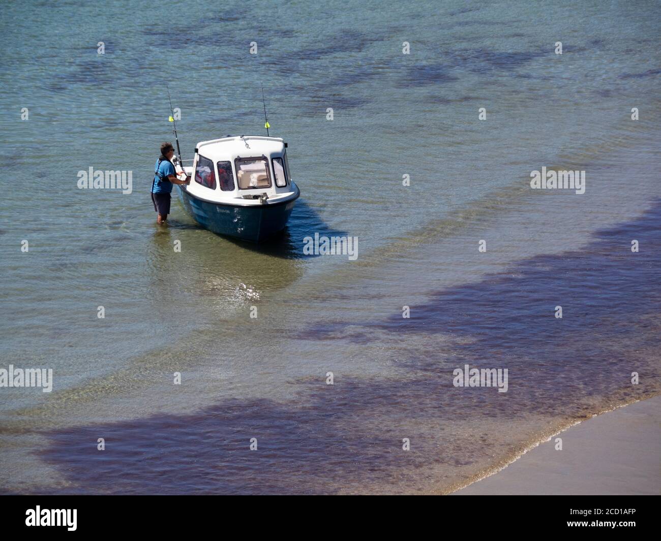 Uomo che tiene una piccola barca da crociera in acque poco profonde sulla spiaggia di Porthcurnick, Cornovaglia, Regno Unito Foto Stock