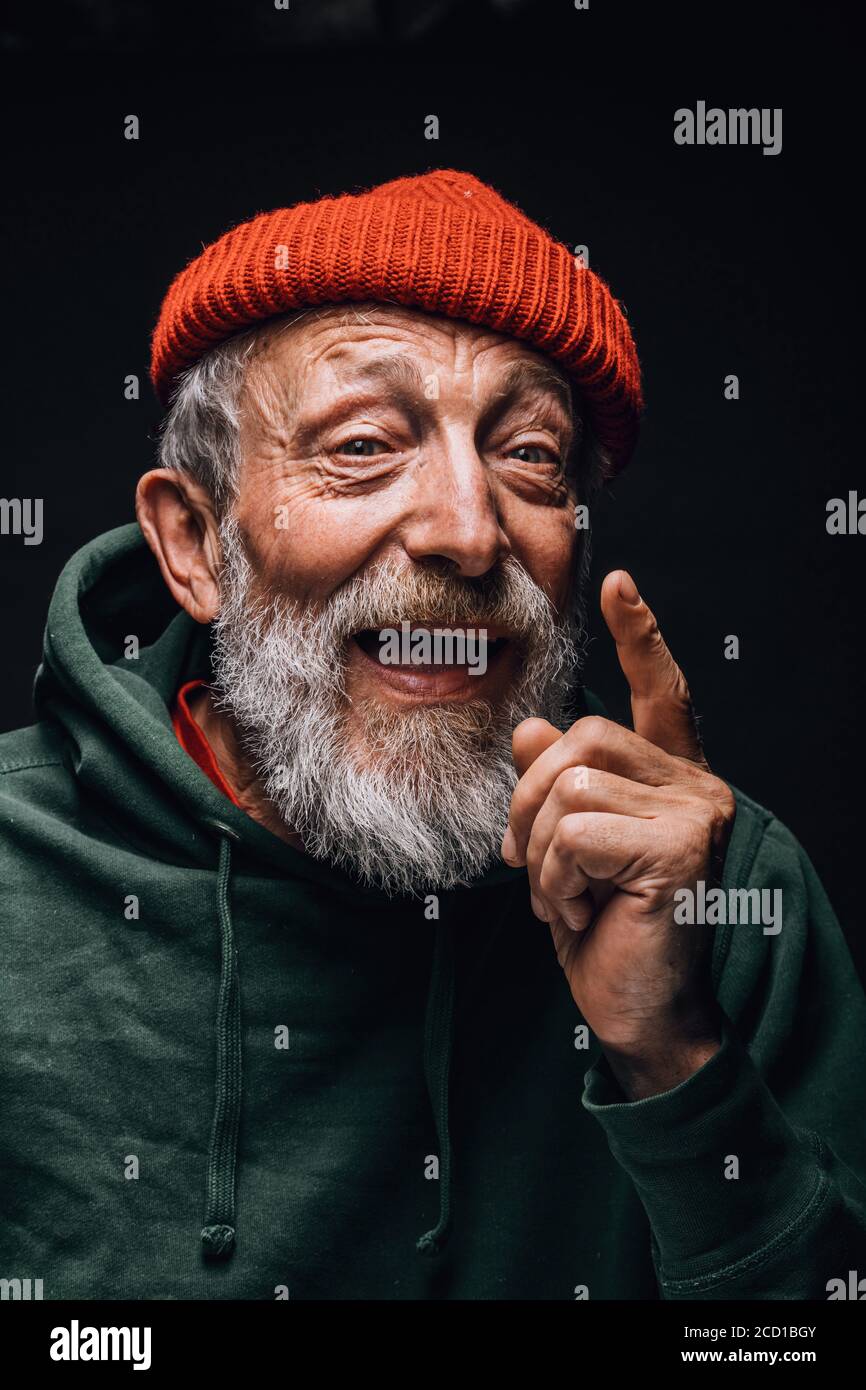 Ritratto di vecchio uomo bearded in cappello arancione con viso rugoso e occhi stanchi esperti che esprimono positività e gioia, ponendosi isolato sopra Foto Stock