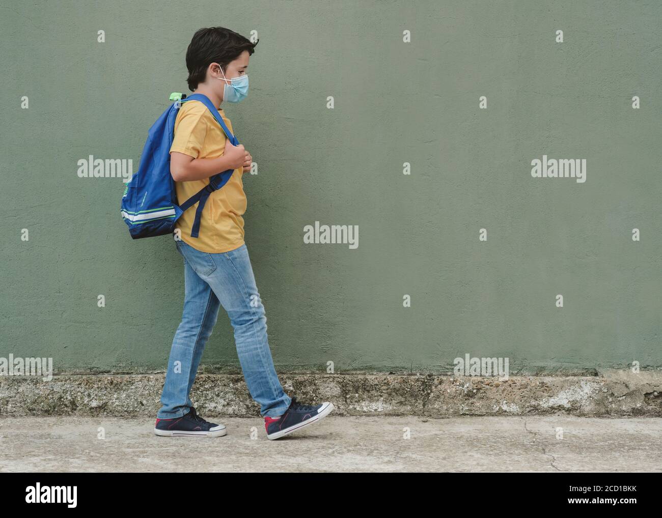 covid-19, bambino con maschera medica e zaino andando a scuola oltre sfondo verde Foto Stock