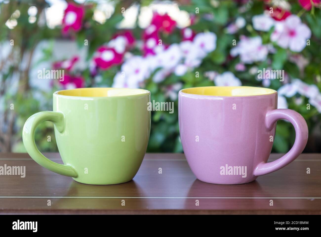 Tazza di caffè mockup su un tavolo da giardino. Tazze bianche di colore  rosa e verde con manico per bevande calde, sfocatura fiore sfondo.  Pubblicità, brandi Foto stock - Alamy