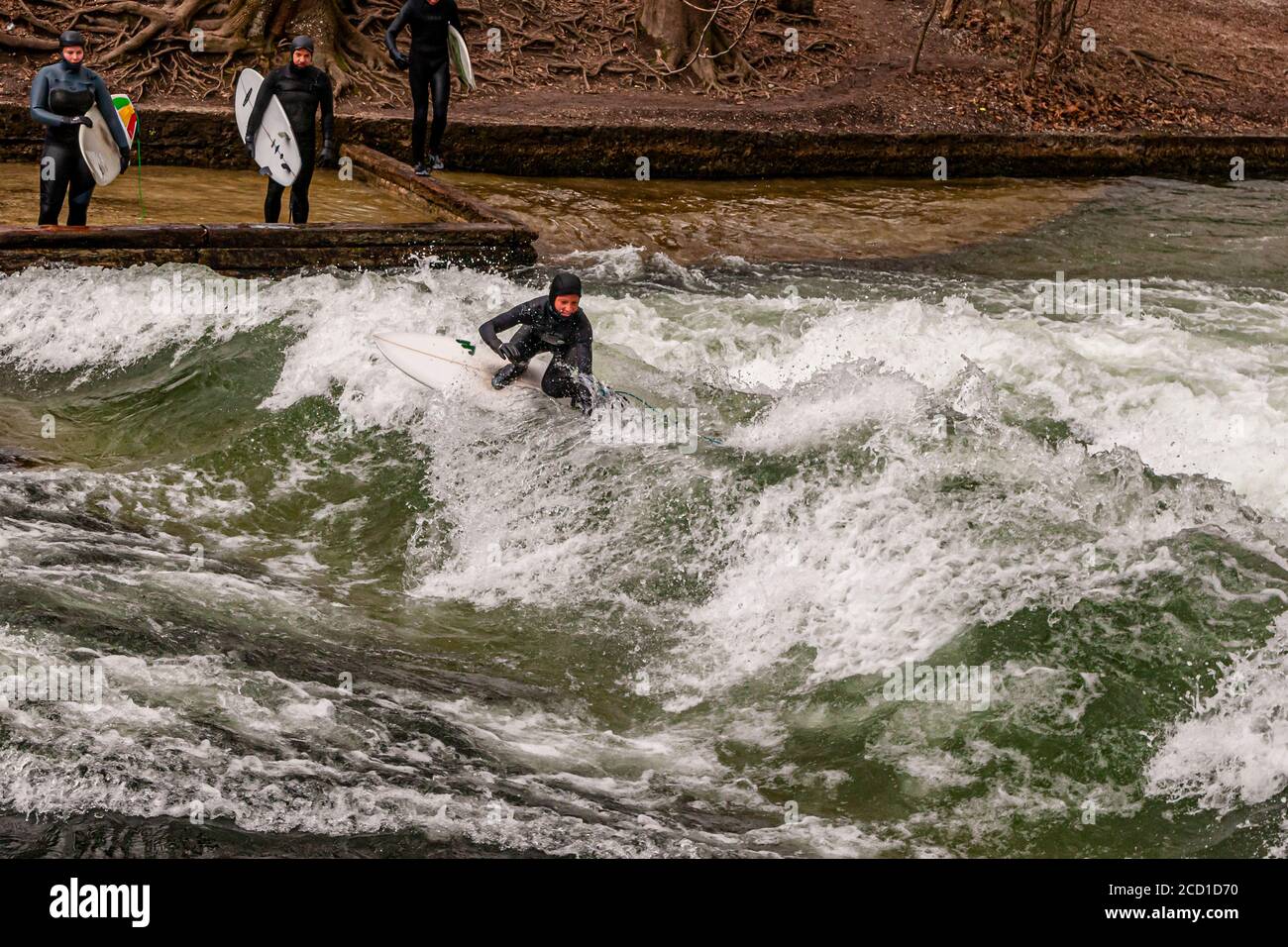 River-Surf sulla Eisbach a Monaco, Germania. L'onda stazionaria può essere surfed per finchè il suo equilibrio tiene e nei periodi occupati una fila dei surfers forma sulla banca Foto Stock