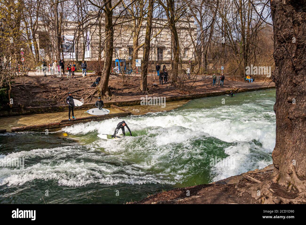 River-Surf sulla Eisbach a Monaco, Germania. L'onda stazionaria può essere surfed per finchè il suo equilibrio tiene e nei periodi occupati una fila dei surfers forma sulla banca Foto Stock