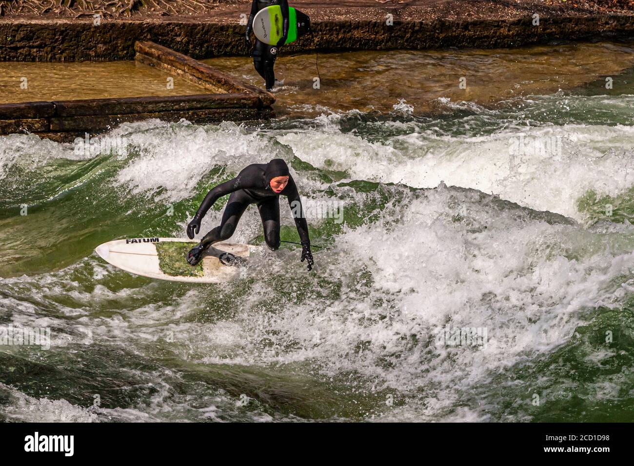 River-Surf sulla Eisbach a Monaco, Germania. L'onda stazionaria può essere surfed per finchè il suo equilibrio tiene e nei periodi occupati una fila dei surfers forma sulla banca Foto Stock