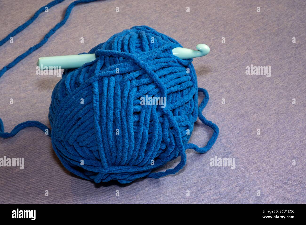 Un gancio a crochet in plastica viene spinto attraverso una grande sfera di filo blu spesso destinata a realizzare coperte. Foto Stock