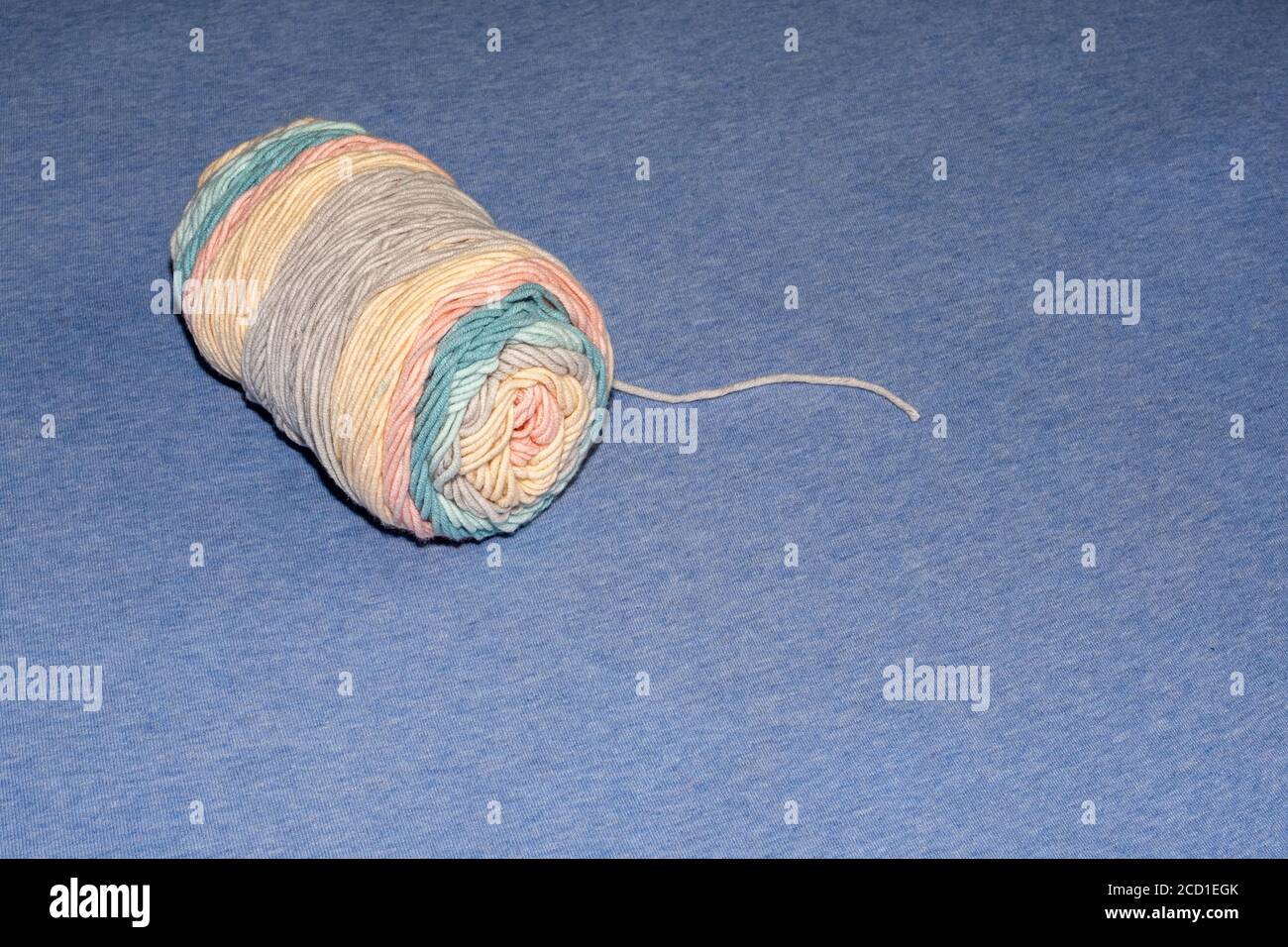 Una matassa di filato strettamente avvolta ha colori blu pastello, rosa e arancio. Il filo giace su una superficie di tessuto, con un unico filo che si estende verso l'esterno. Foto Stock