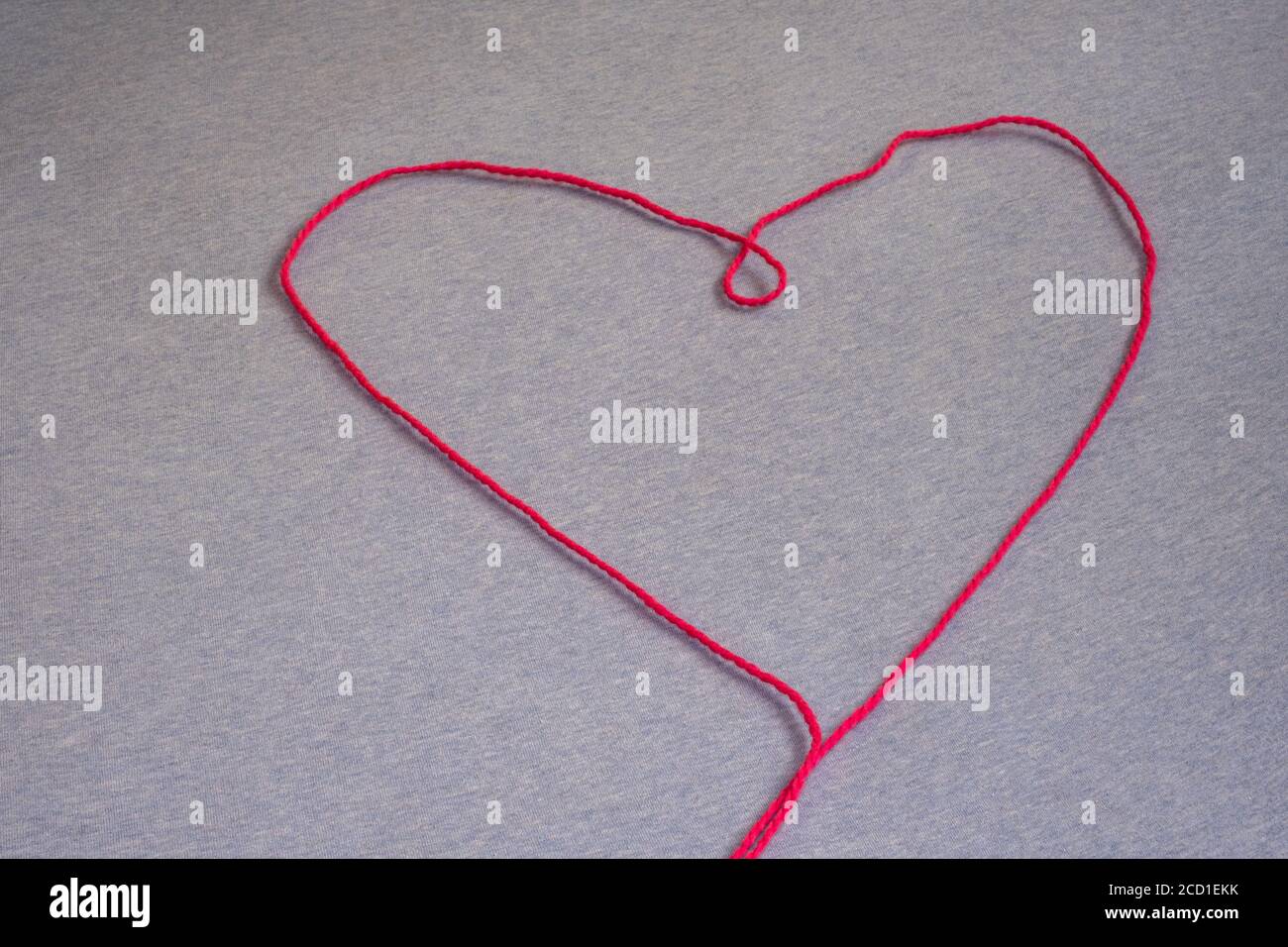 Un unico filo di filo rosa forma la forma di un cuore, disposto su una superficie piana del tessuto. Foto Stock