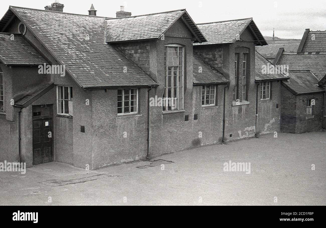 Anni '50, quadro storico di questa epoca che mostra una parte della scuola primaria e parco giochi del villaggio vittoriano, Llandyssil, Powys, Galles. Costruito nel 1866, è stato progettato da Thomas Henry Wyatt, un architetto anglo-irlandese, che ha avuto una carriera distinta, essendo stato eletto presidente del Royal Institute of Briitsh Architects nel 1870 ed è stato ricevuto dalla Royal Gold Medal per l'architettura nel 1873. La scuola si è chiusa nel 1950 e parte di essa è stata salvata solo nel 2010 da una campagna di raccolta fondi per far diventare la sala scolastica un centro comunitario locale. Foto Stock