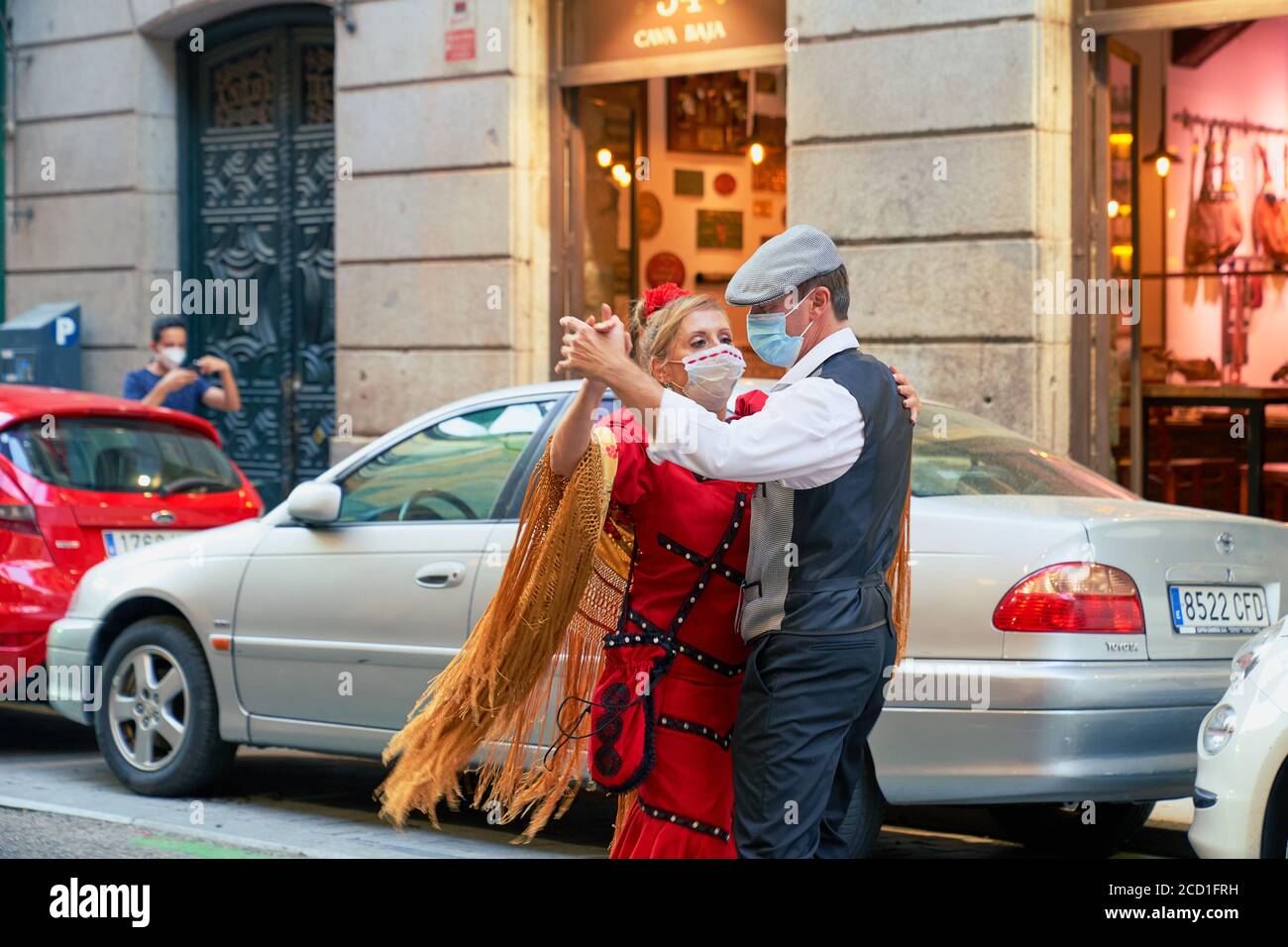 Uomo con cappello piatto e donna in abito flamenco rosso, entrambi mascherati, ballano la chotis a La Latina, Madrid, agosto 2020 Foto Stock