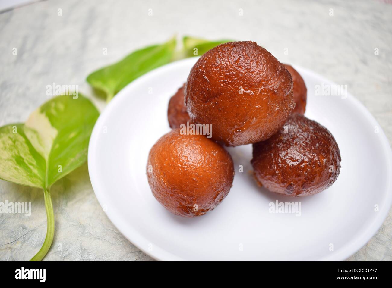 Primo piano di Gulab jamun dolce indiano su sfondo bianco su piatto bianco. Decorato con foglie di montana. Foto Stock