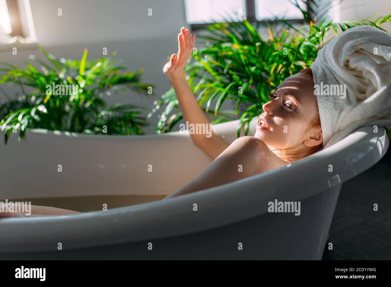 Bella giovane donna coccolando il corpo in acqua, prendendo bagno con oli minerali in un'atmosfera rilassante della zona termale dell'hotel al mattino soleggiato Foto Stock