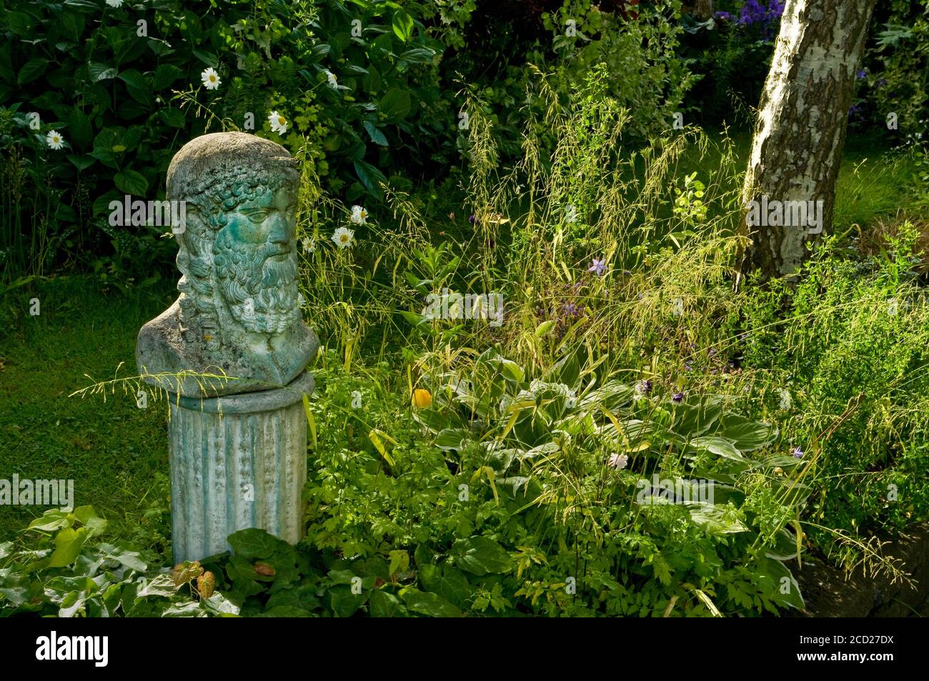 Piccola statua in stile greco di una testa su una colonna vicino Un letto a fiori in un giardino all'inglese Foto Stock