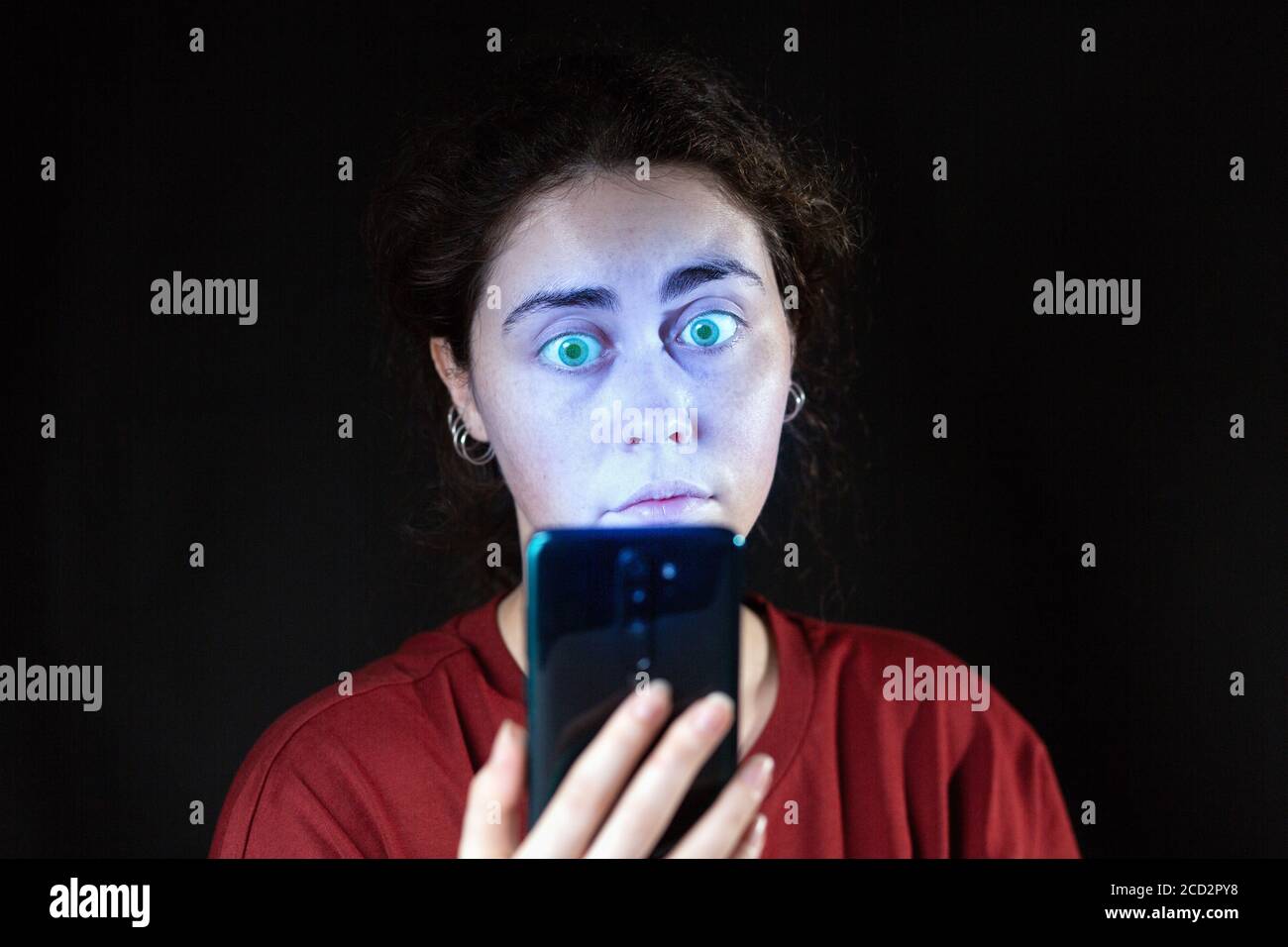 Ritratto di una donna che guarda il suo cellulare come una zombie. Sfondo nero. Spazio di copia. Il concetto di dipendenza online. Foto Stock